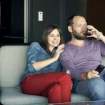 young-couple-watching-tv-drinking-wine-and-laughing-on-sofa-at-home_roofy8ig__F0013_Fotor